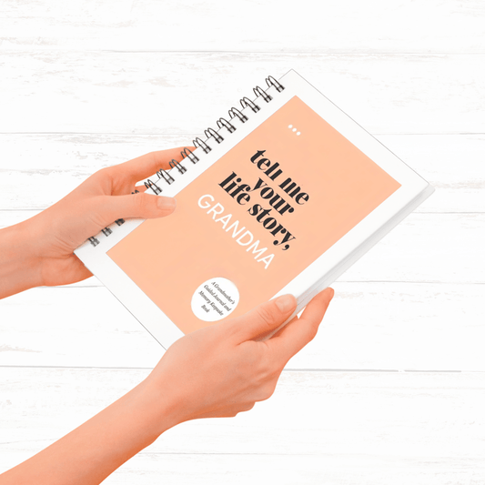 Person holding a book titled 'Tell me your life story, Grandma' on a white wooden surface