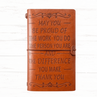 Brown leather notebook with engraved text on a white wooden background