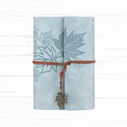 Light blue notebook with leaf design and leather strap on a white wooden background
