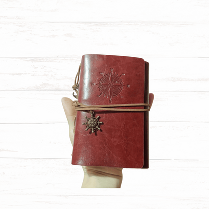Red leather journal with compass design on a white wooden surface